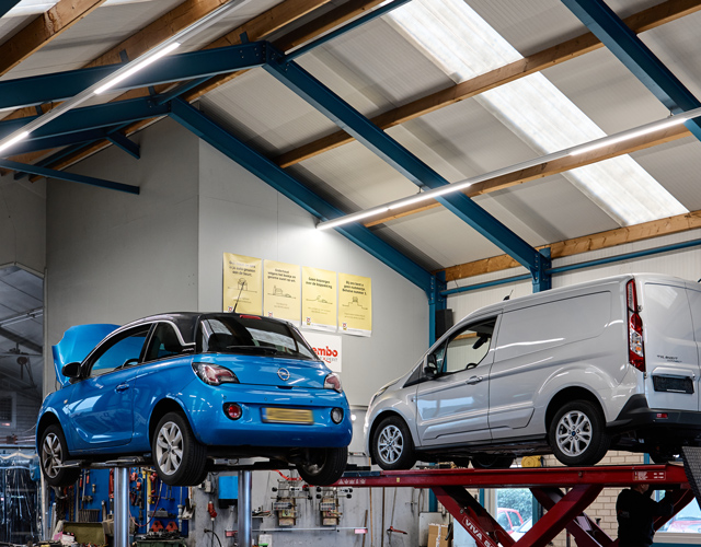Blauwe Opel Adam en een Ford-bus op schaarbruggen in de werkplaats