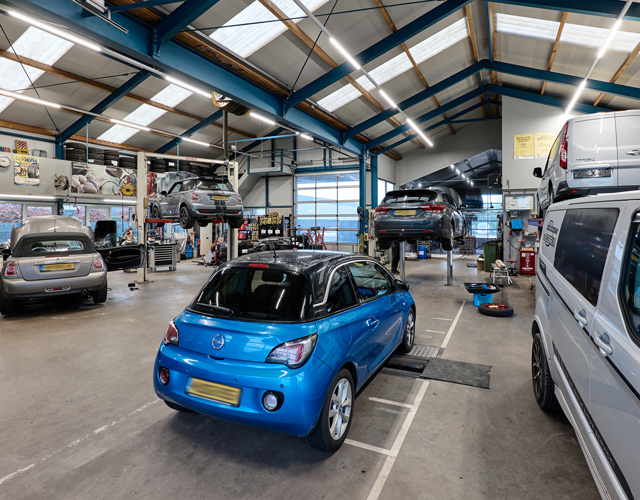 Brede blik door de werkplaats met bruggen, een blauwe Opel Adam en een Ford-bus