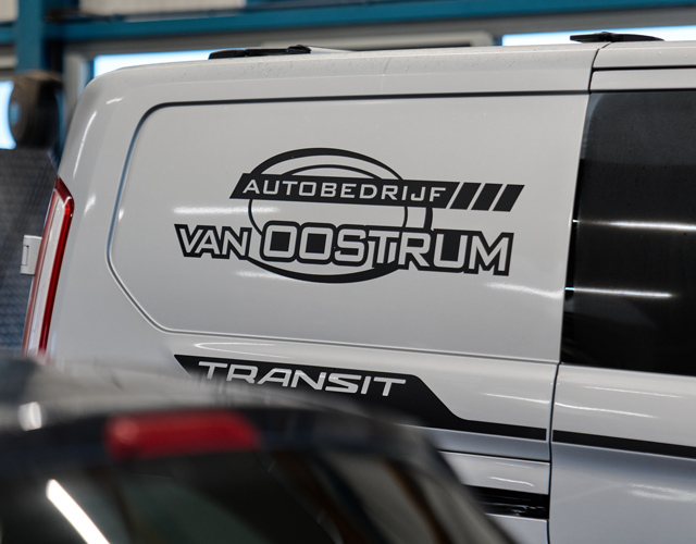 Het logo van Autobedrijf Van Oostrum op de zijkant van een Ford Transit-bedrijfsbus